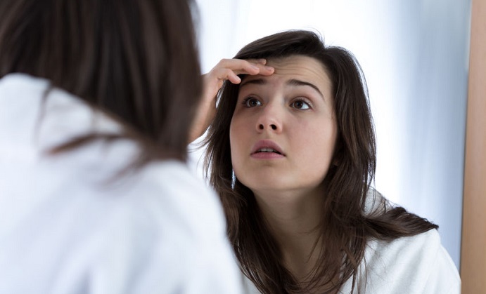 girl having problems with skin looking in the mirror