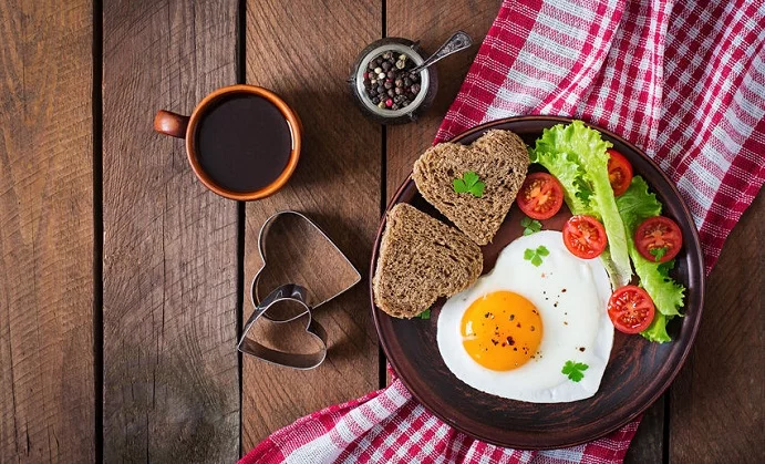 breakfast on valentine's day - fried eggs and bread in the shape of a heart and fresh vegetables. top view