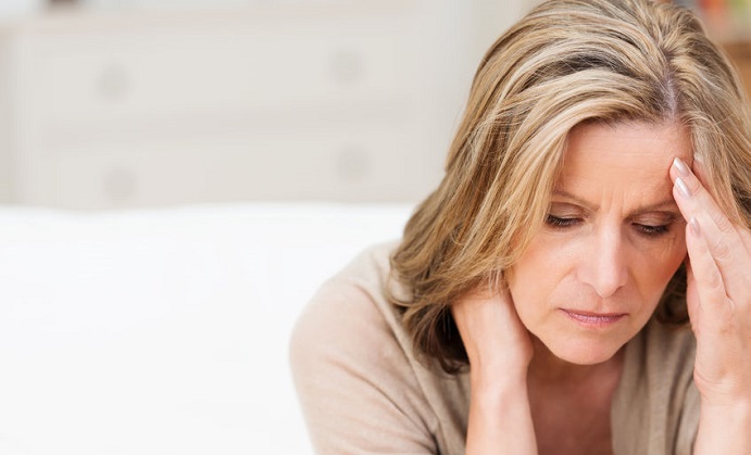 woman suffering from stress or a headache grimacing in pain as she holds the back of her neck with her other hand to her temple, with copyspace