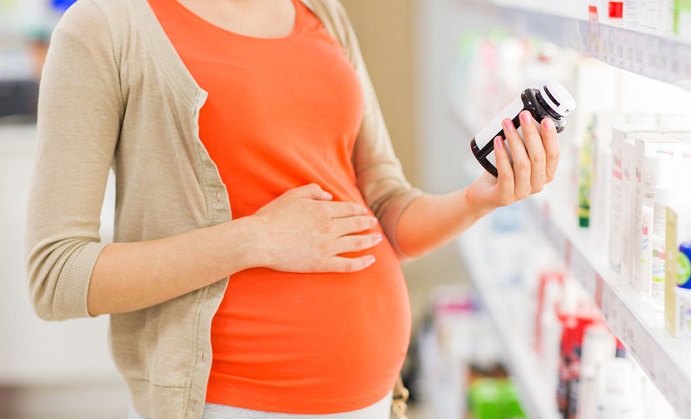 pregnancy, medicine, pharmaceutics, health care and people concept - close up of pregnant woman reading label on medication jar at pharmacy